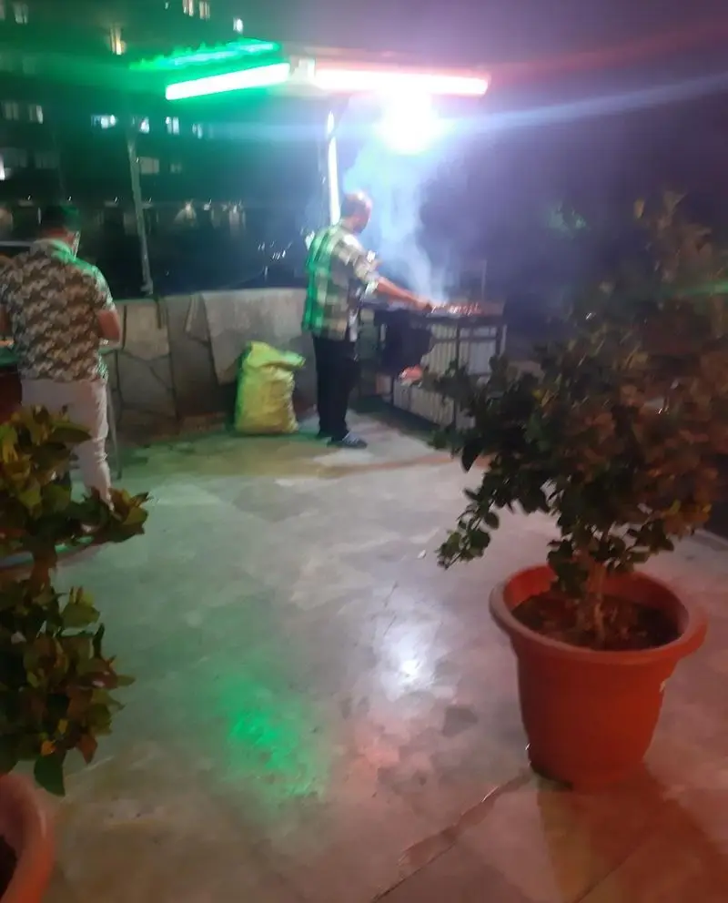 نمایی از فضای دلنشین و شبانه جگرسرای بهنام و برادران، مردی در حال پخت کباب جگر تازه روی گریل در محیطی باز و سرسبز.