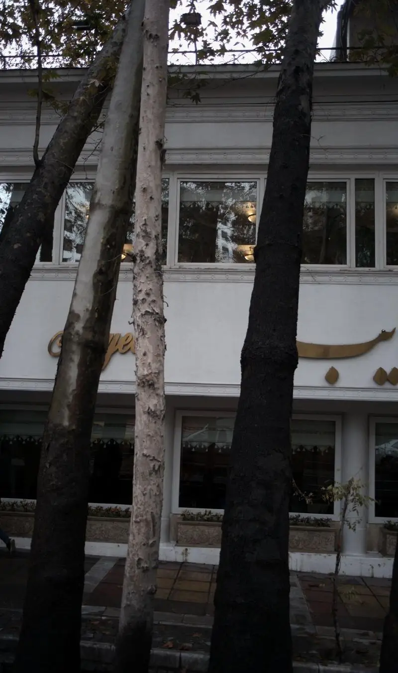 تصویر نمای بیرونی رستوران نایب زعفرانیه در منطقه زعفرانیه تهران با درختان بلند در پیش‌زمینه و تابلو طلایی نام رستوران.