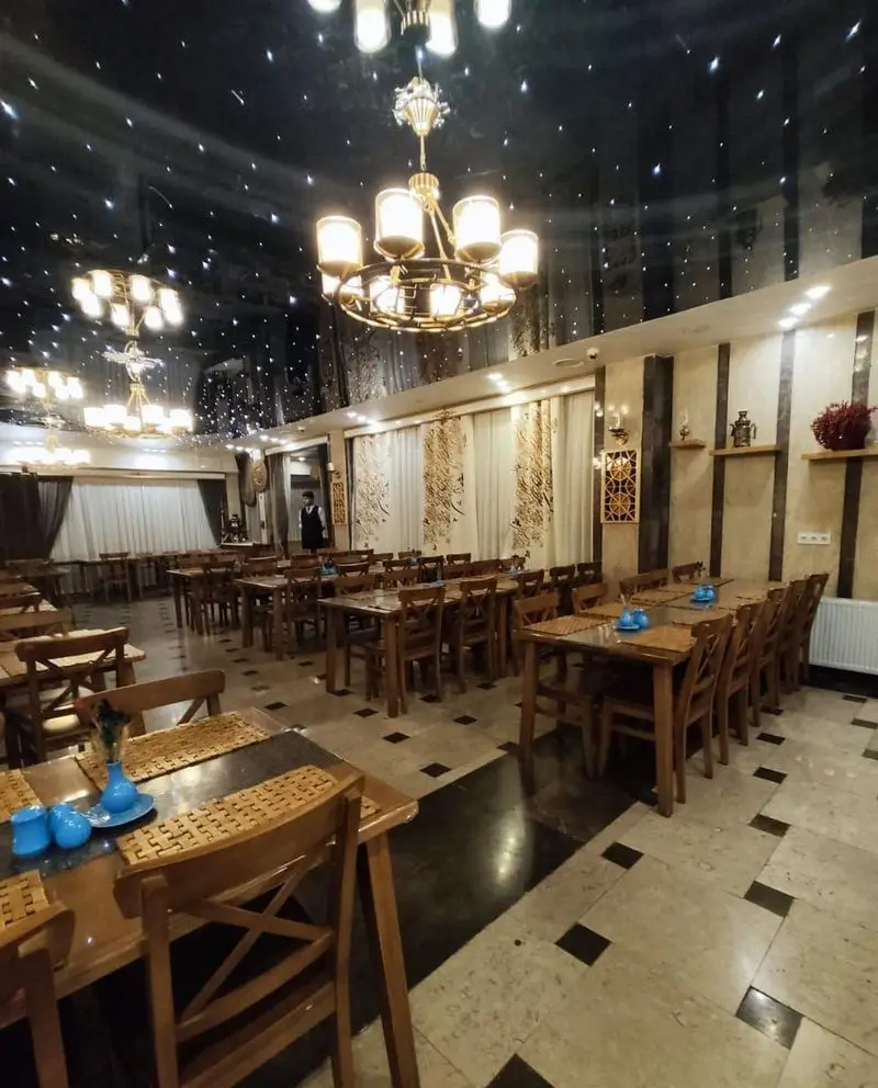 فضای داخلی شیک و مدرن رستوران مسینه با سقف کهکشانی خیره‌کننده، لوسترهای طلایی و چیدمان میز و صندلی چوبی برای تجربه‌ای دلپذیر.