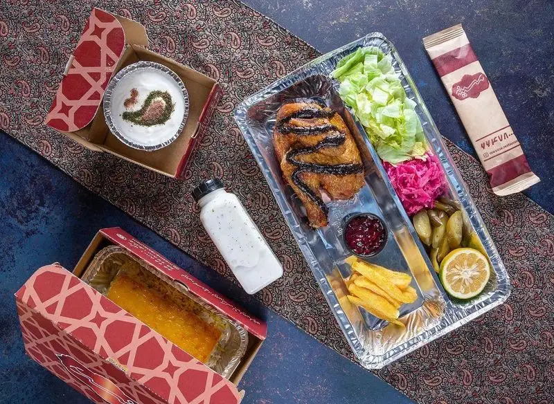 سینی غذای بیرون بر رستوران مسینه شامل جوجه کباب، سیب زمینی، سالاد، ترشی، ماست، نوشیدنی دوغ و ته دیگ زعفرانی.