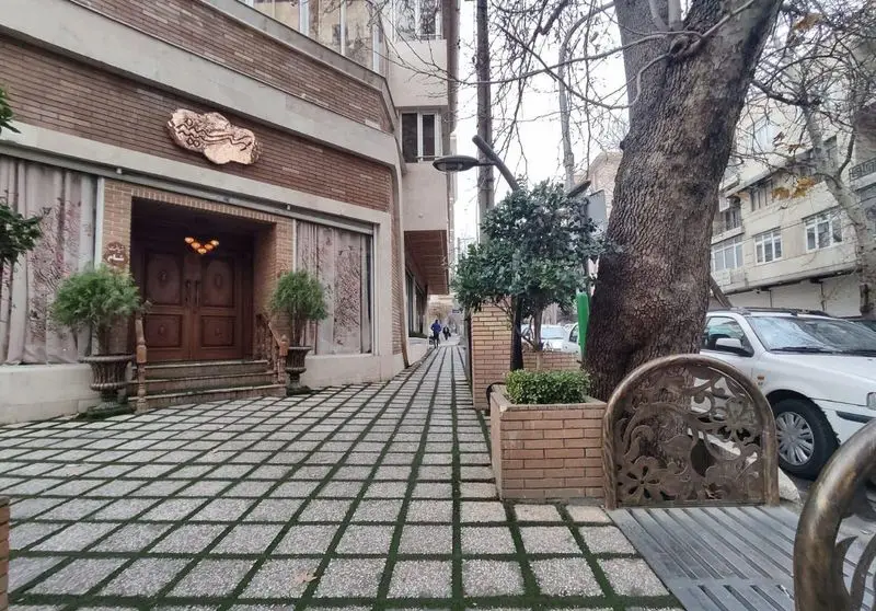 نمای بیرونی رستوران مسینه با تابلوی مسی زیبا، ورودی چوبی، گلدان‌ها و پیاده‌رو مدرن. فضایی دنج و شیک برای تجربه غذایی دلپذیر.