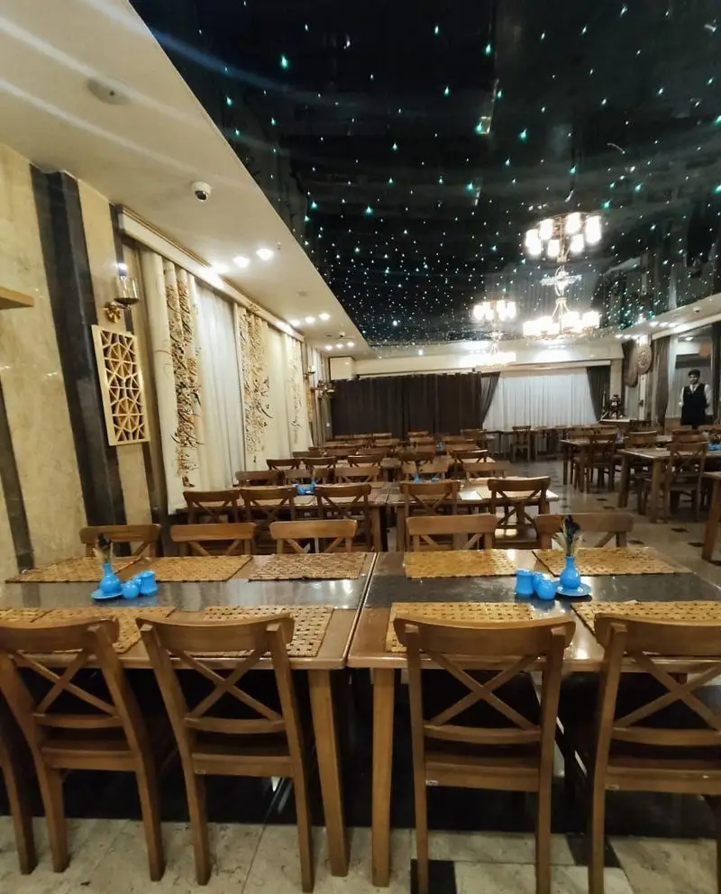 نمایی از فضای داخلی رستوران مسینه با سقف کهکشانی درخشان، میز و صندلی‌های چوبی و دکوراسیون زیبای دیوارها برای تجربه‌ای فراموش‌نشدنی.