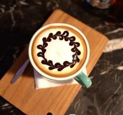 فنجان قهوه اسپرسو با لاته آرت خیره کننده از طرح برگ و پیچک شکلاتی روی میز چوبی در کافه رستوران سنتی قصر ایرانیان.
