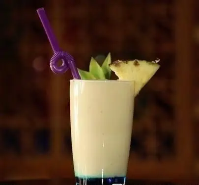 نوشیدنی آناناس خنک و دلنشین در لیوانی بلند با نی بنفش، تزئین شده با برگ و میوه آناناس، از کافه رستوران سنتی قصر ایرانیان.