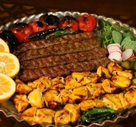 سینی کباب کوبیده و جوجه کباب لذیذ در کافه رستوران سنتی قصر ایرانیان، شامل گوجه کبابی و مخلفات تازه. غذای اصیل ایرانی.