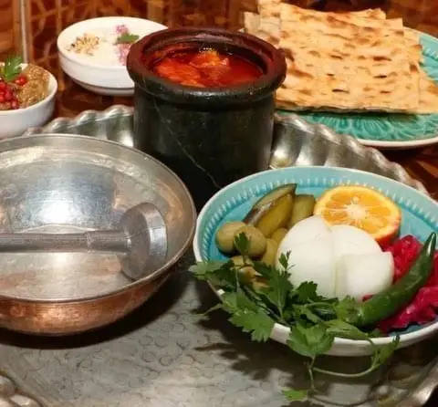 یک میز پر از دیزی سنگی با نان تازه، سبزی و ترشیجات، و سایر مخلفات خوشمزه در کافه رستوران سنتی قصر ایرانیان، بهترین غذای سنتی.