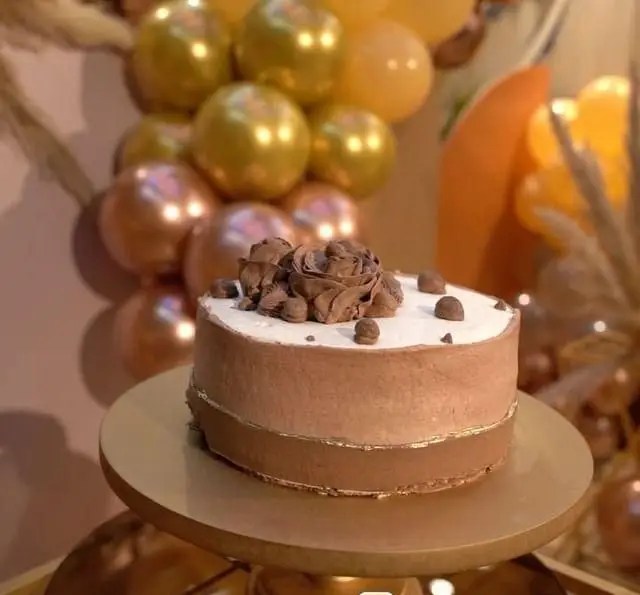 کیک شکلاتی مجلل و خاص کافه رستوران سنتی قصر ایرانیان، با تزئینات رز شکلاتی، نوار طلایی و بادکنک‌های رنگی جشن در پس‌زمینه.