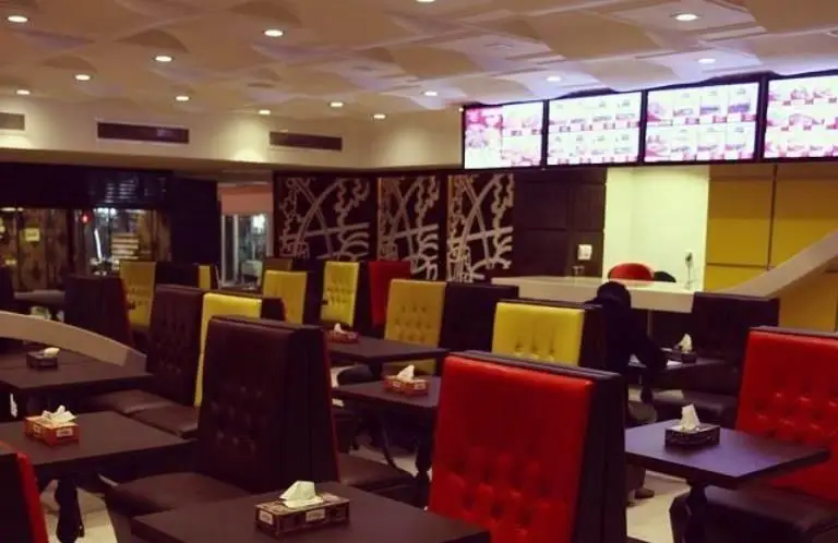 فضای دلنشین رستوران مازستا با میز و صندلی‌های راحتی در رنگ‌های قرمز و زرد. دکوراسیون مدرن، محیطی ایده‌آل برای صرف غذا و منو دیجیتال.