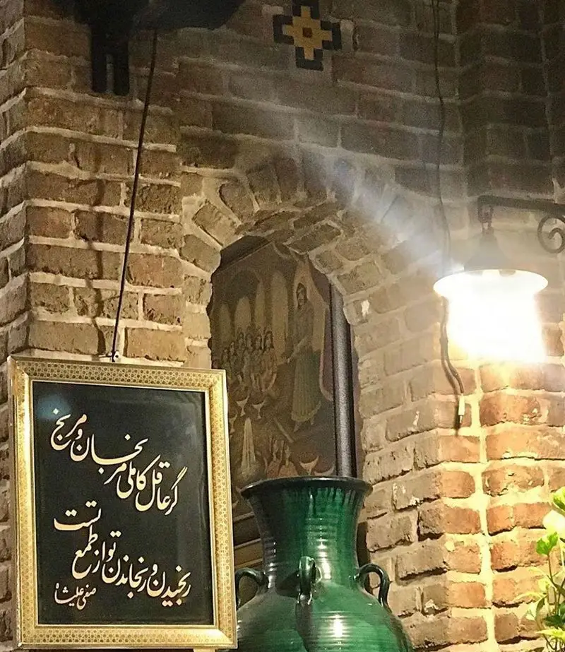 تصویری از فضای داخلی دلنشین و دنج رستوران آذری ایرانی، شامل دیوارهای آجری، تابلوی خطاطی، گلدان سنتی و نقاشی دیواری.