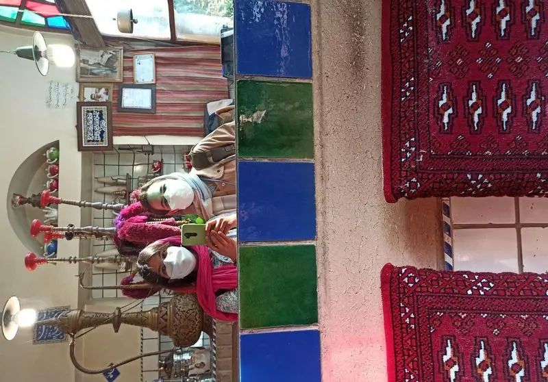 فضای داخلی دنج رستوران سنتی ایرانی آذری، با حضور مشتریان دارای ماسک، قلیان‌های طرح‌دار، کاشی‌های فیروزه‌ای و فرش‌های دستباف.