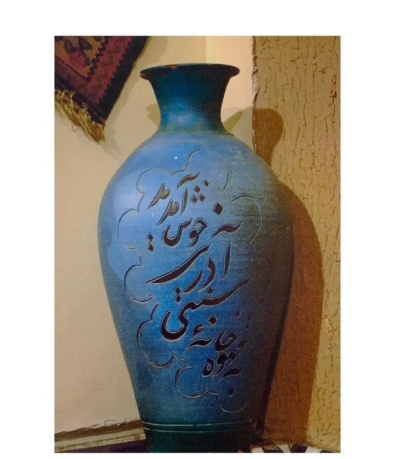 گلدان سفالی آبی رنگ دست‌ساز با خطاطی زیبای فارسی "مهمان حبیب خداست"، نمادی از مهمان‌نوازی اصیل ایرانی در دکوراسیون رستوران آذری.