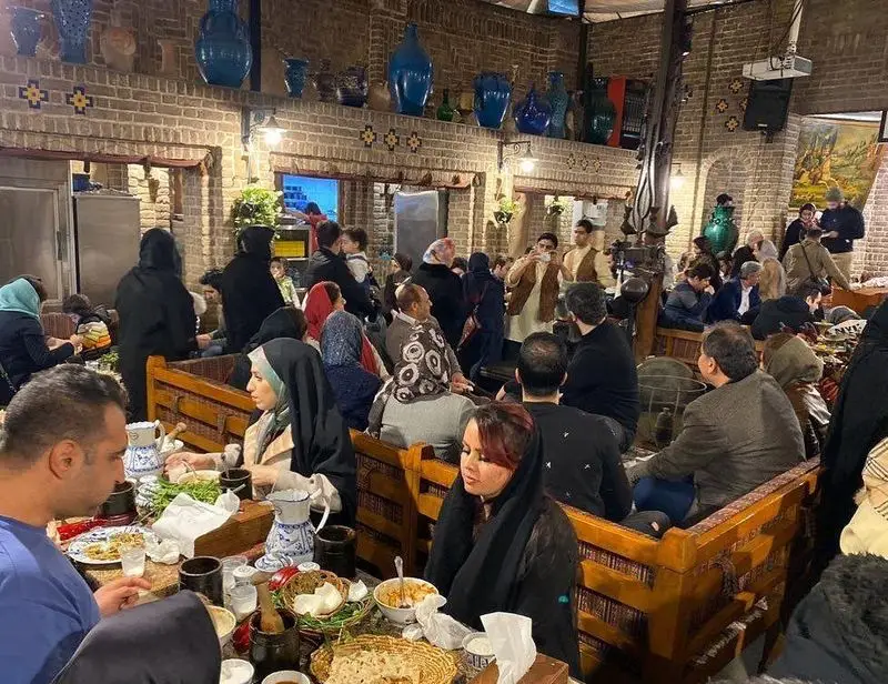 نمای داخلی رستوران ایرانی آذری با دکوراسیون سنتی و مشتریانی که دور هم جمع شده و مشغول صرف غذای لذید ایرانی هستند.