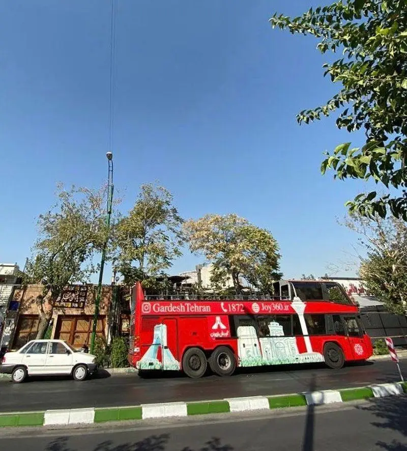 اتوبوس گردشگری دوطبقه قرمز رنگ در خیابان‌های تهران، نمادی از پایتخت. پس از گشت‌وگذار، از طعم لذیذ غذای ایرانی در رستوران آذری لذت ببرید.