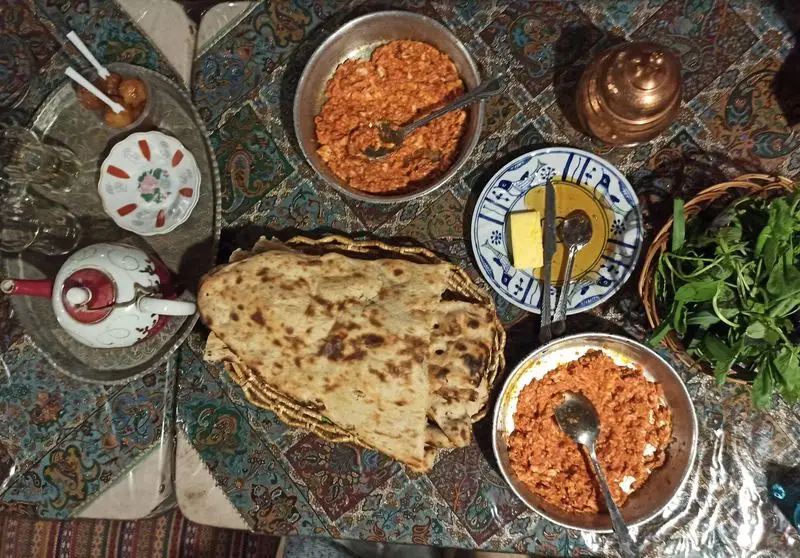 میز غذای لذیذ رستوران ایرانی آذری: نان داغ، املت محلی، سبزی خوردن تازه، کره، و چای سنتی برای مهمانان.