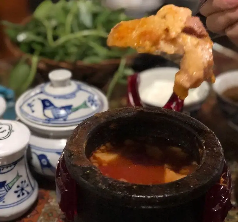 سرو غذای سنتی آذری در رستوران ایرانی آذری: تکه‌ای گوشت یا توفو در حال در آمدن از دیزی سفالی با آبگوشت قرمز و سبزی خوردن تازه.