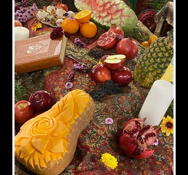 سفره رنگین شب یلدا یا هفت سین نوروز در رستوران ایرانی آذری با میوه‌های تازه و حکاکی‌شده، کتاب و شمع.