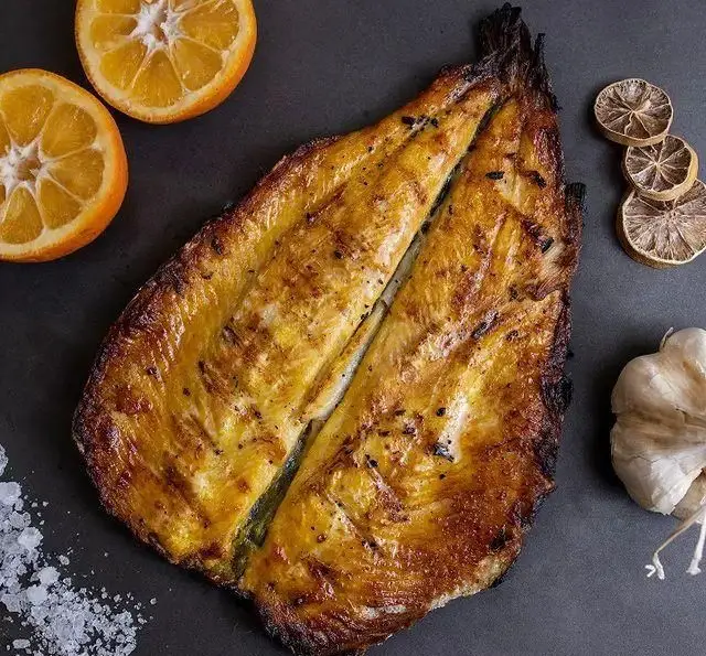 ماهی گریل شده خوشرنگ و اشتهاآور ساطور با برش پروانه‌ای، همراه با پرتقال تازه، لیمو خشک، سیر و نمک دریایی. غذای دریایی عالی.