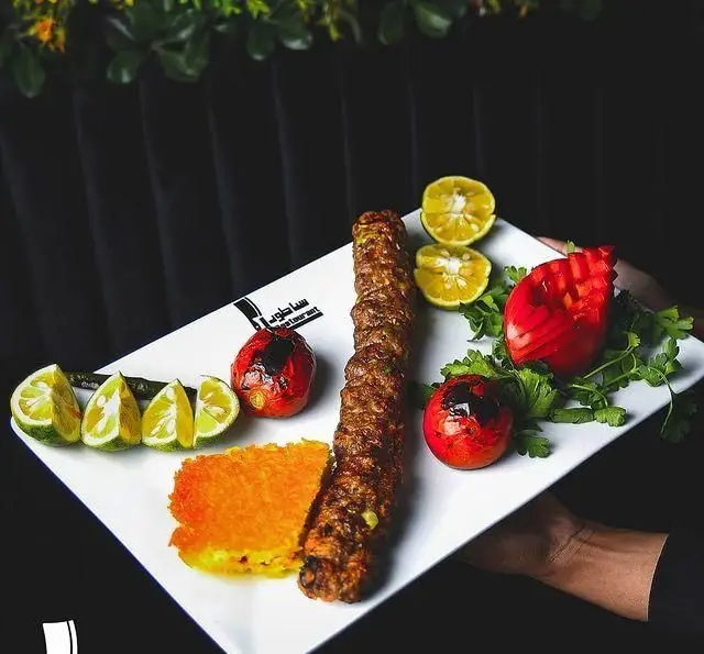 کباب کوبیده خوشمزه رستوران ساطور، همراه با برنج زعفرانی، گوجه کبابی، لیمو و سبزیجات. تجربه ای اصیل از غذای ایرانی.