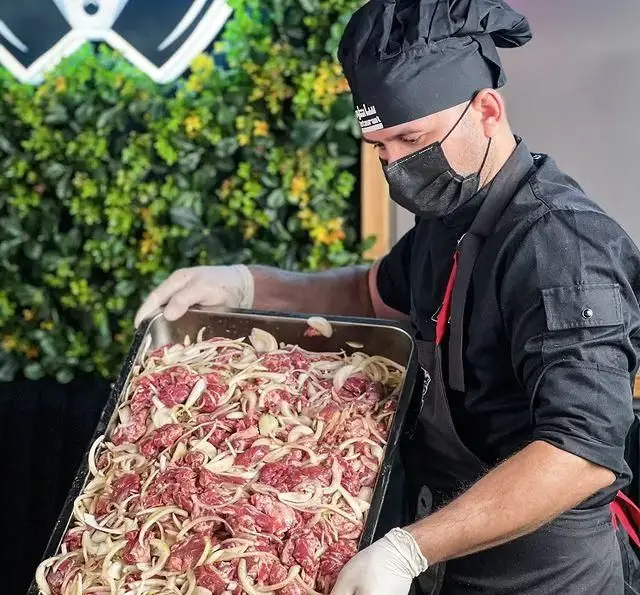 سرآشپز رستوران ساطور در حال آماده‌سازی گوشت کباب با پیاز تازه در سینی؛ تاکید بر کیفیت و بهداشت در طبخ غذاهای اصیل.