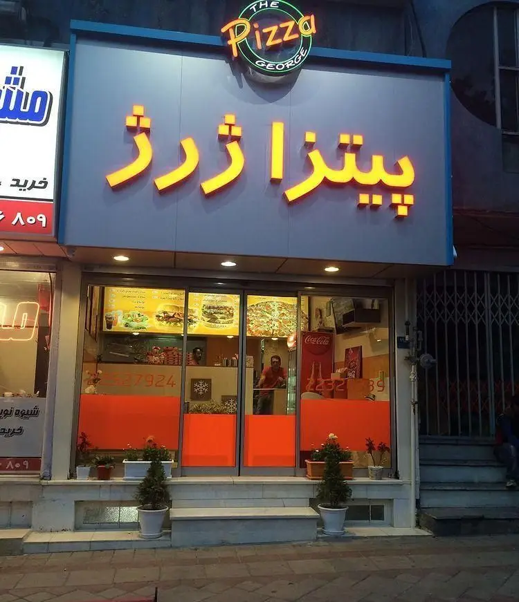 تصویری از نمای بیرونی مغازه فست فود پیتزا ژرژ با تابلوی نئون برجسته "THE Pizza GEORGE" و منوی غذایی متنوع در ویترین، شامل پیتزا و برگر.