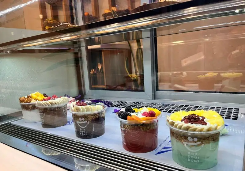 مجموعه‌ای از کاسه‌های آسایی تازه و متنوع "آسایی کاسه روح" شامل طعم‌های میوه‌ای، شکلاتی و دیگر ترکیب‌ها با تزیینات لذیذ در ویترین فروشگاه.