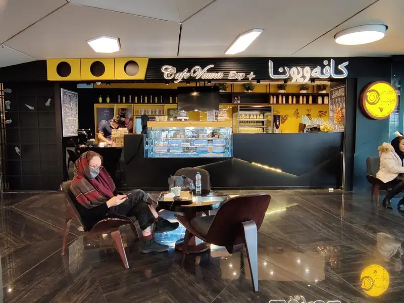 نمای داخلی کافه ویونا فود کورت رویال با دکوراسیون مدرن مشکی-زرد، پیشخوان شلوغ و مشتریان در حال استراحت در محیطی دنج و روشن.