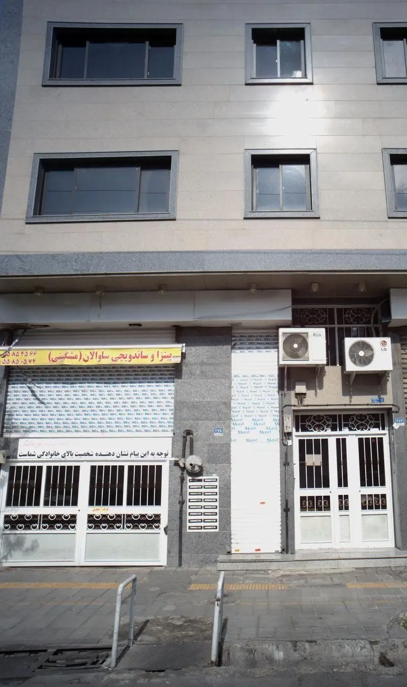 نمای بیرونی فروشگاه پیتزا و ساندویچ ساوالان (مشگینی) با تابلوی زرد، کرکره‌های بسته و نمای آپارتمان مسکونی در بالای آن.