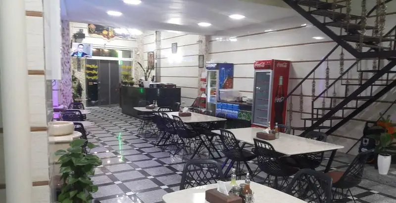 فضای داخلی طباخی طهران: میز و صندلی‌های شیک، کفپوش شطرنجی، یخچال نوشیدنی و پله‌های فلزی. محیطی تمیز و آماده پذیرایی.