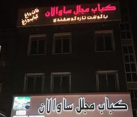 نمایی شبانه از سردر رستوران کباب مجلل ساوالان با تابلوهای درخشان، ارائه دهنده کباب داغ و نان داغ با گوشت تازه گوسفندی.