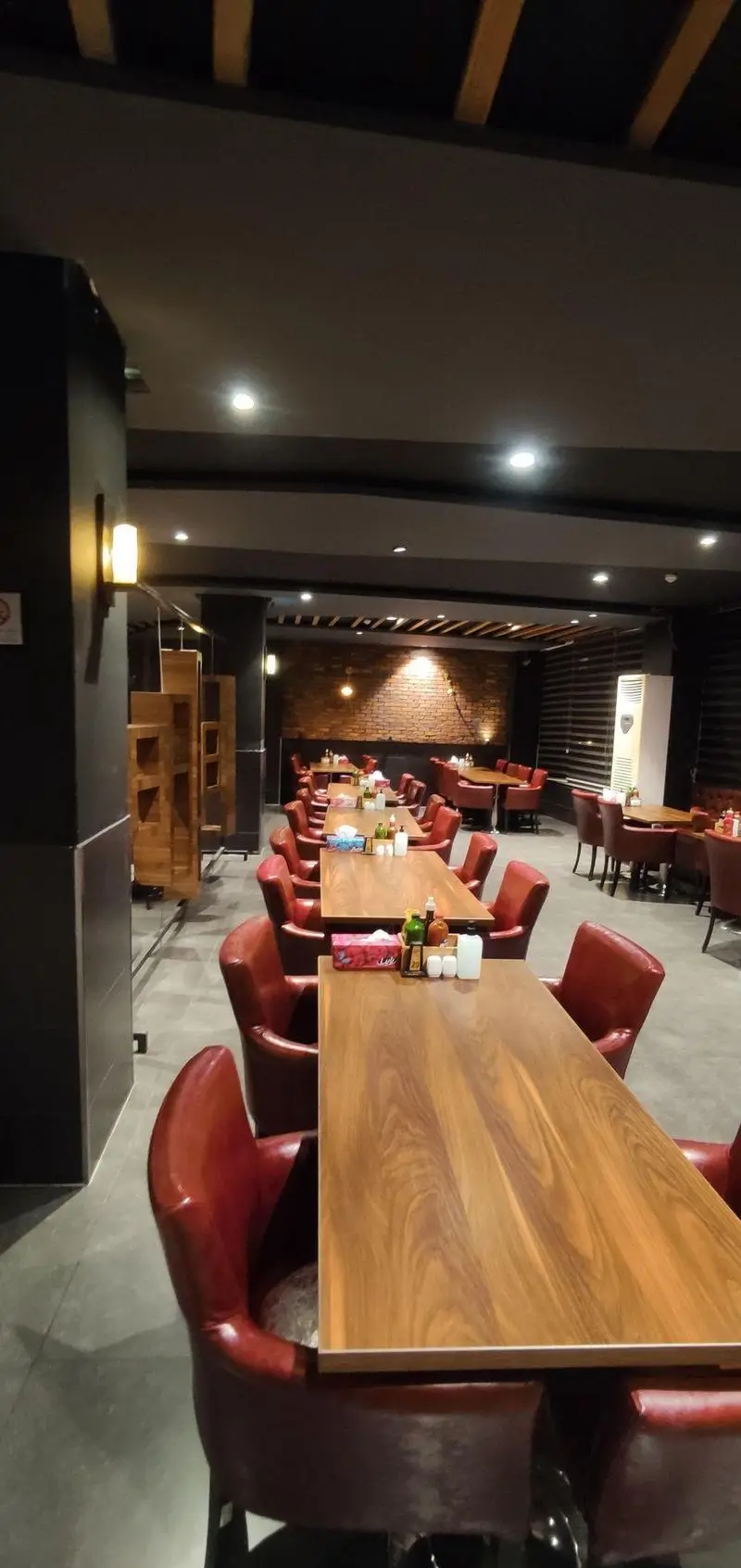 فضای داخلی رستوران ایتالیایی مریخ با چیدمان منظم میزهای چوبی و صندلی‌های قرمز راحتی، محیطی گرم و دلنشین. دکوراسیون آجری و نورپردازی مدرن.