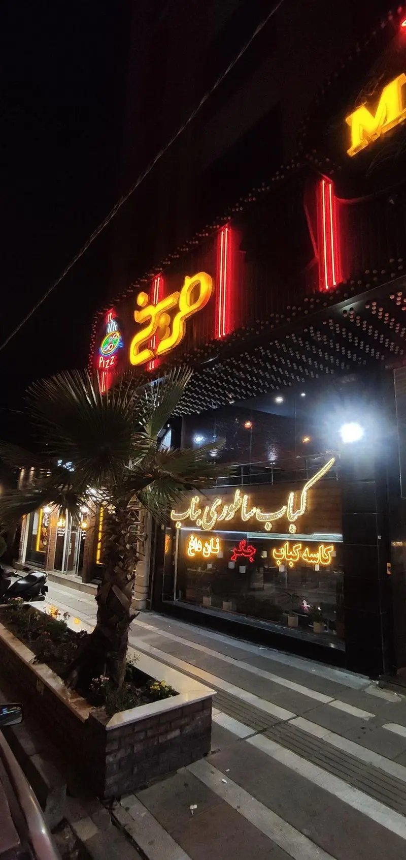 رستوران مریخ در شب با تابلوی نئونی زرد و قرمز 'مریخ' و 'Pizz'، و نمایش 'کباب ساطوری بناب، کاسه کباب، جگر، نان داغ' بر روی شیشه.