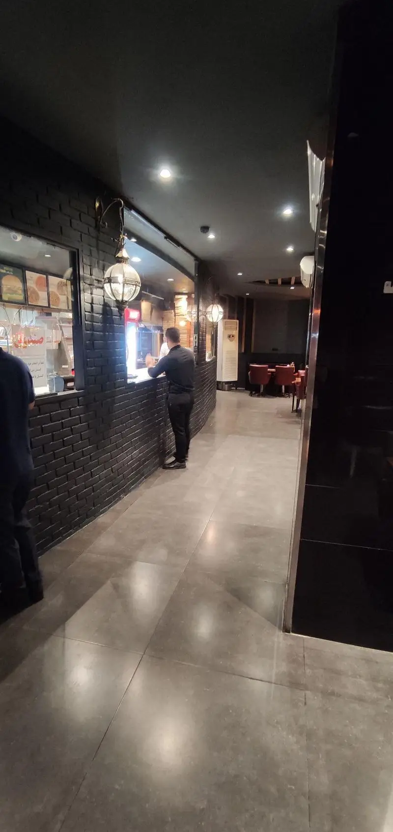 فضای داخلی شیک و مدرن رستوران ایتالیایی مریخ با کانتر خدماتی، دیوار آجری مشکی، نورپردازی گرم و محیطی دلنشین برای صرف غذا.