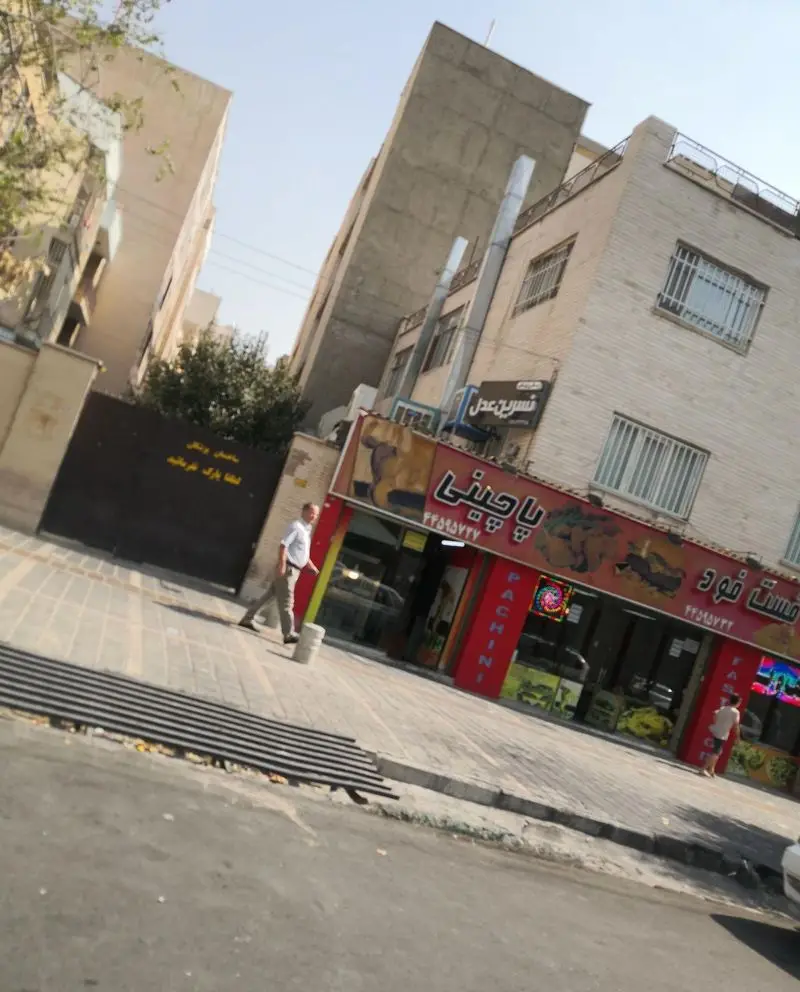 تصویری از نمای بیرونی فست فود پاچینی با تابلوی قرمز رنگ، مشتریان و مردم در حال عبور در یک روز آفتابی در خیابان شلوغ شهر.