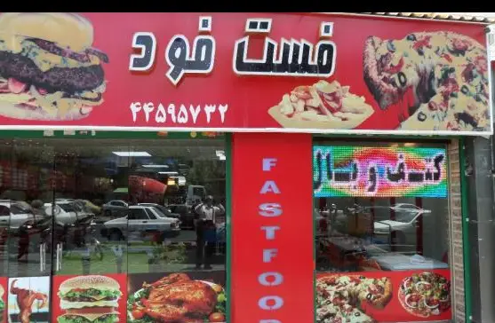 تصویری از یک فست فود پاچینی با تابلوی قرمز رنگ "فست فود" و شماره تماس، شامل تصاویر جذاب همبرگر، پیتزا و مرغ سوخاری که مشتریان را جذب می‌کند.
