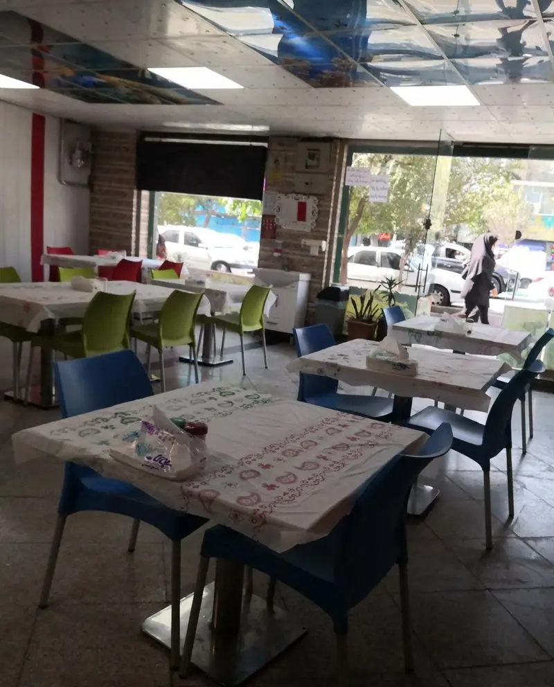 فضای داخلی تمیز و دلنشین فست فود پاچینی، شامل میز و صندلی‌های چیده شده و آماده برای مشتریان با نمای بیرونی خیابان.