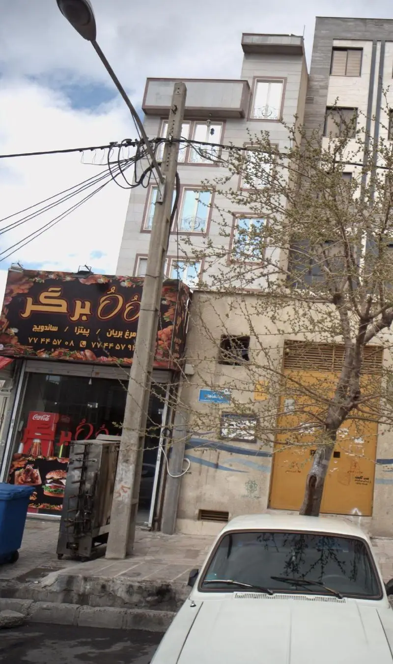 تابلو برگر OُOُ با منوی مرغ بریان، پیتزا و ساندویچ، شماره‌های تماس ۷۷۴۴۵۷۰۸ و ۷۷۴۴۵۷۹۱ در نمای خیابان مغازه.