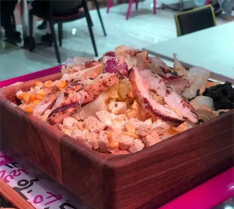 سالاد مرغ گریل لذیذ با سس مخصوص، کروتون، ذرت، زیتون و سبزیجات تازه، سرو شده در کاسه چوبی در فست فود مازی فود.