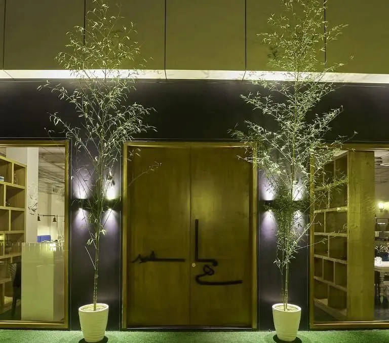 ورودی شیک و مدرن رستوران ماهی سفید با درب طلایی بزرگ، گیاهان بامبو در گلدان‌های سفید و نورپردازی دلنشین.