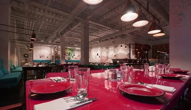 نمای داخلی رستوران ماهی سفید با طراحی مدرن و شیک، شامل میزهای قرمز رنگ با چیدمان زیبا، نورپردازی صنعتی و مبلمان فیروزه‌ای دلنشین.