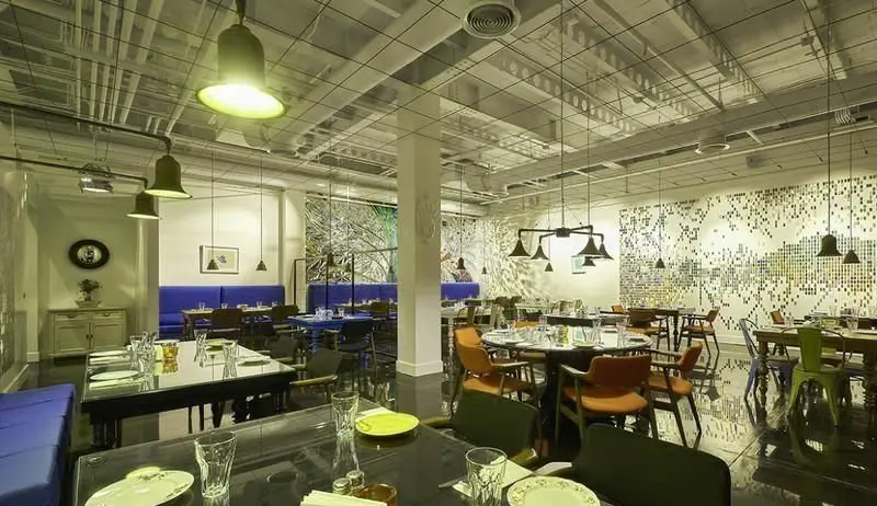 فضای داخلی شیک و مدرن رستوران ماهی سفید، با چیدمان متنوع میز و صندلی‌ها، نورپردازی خلاقانه و دکوراسیون دیواری هنری برای تجربه‌ای دلپذیر.