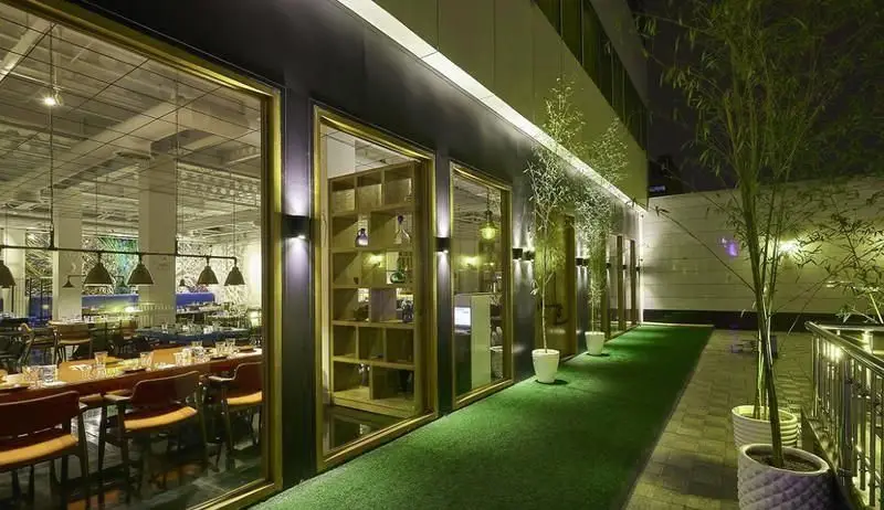 رستوران ماهی سفید، نمایی جذاب از فضای مدرن و شیک در شب. دکوراسیون داخلی با میزهای چوبی، همراه با فضای سبز و نورپردازی حرفه‌ای بیرونی.