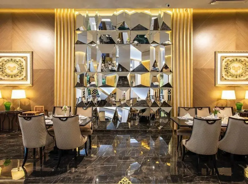 دکوراسیون داخلی مجلل و زیبای رستوران ماهان شاندیز شریعتی. فضای آرام با میز و صندلی‌های شیک، دیوار آینه‌ای سه‌بعدی و کفپوش براق.