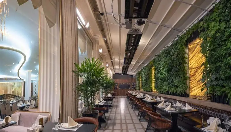 فضای داخلی شیک و مدرن رستوران ماهان شاندیز شریعتی با میز و صندلی‌های چوبی، دیوار سبز و سقف جمع‌شونده برای تجربه غذاخوری دلنشین.