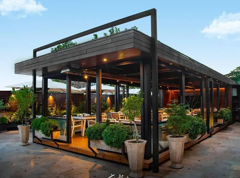 فضای باز شیک و دنج رستوران ماهان شاندیز شریعتی، با طراحی مدرن چوبی و فلزی، میز و صندلی‌های راحت و فضای سبز دلنشین برای صرف غذا.