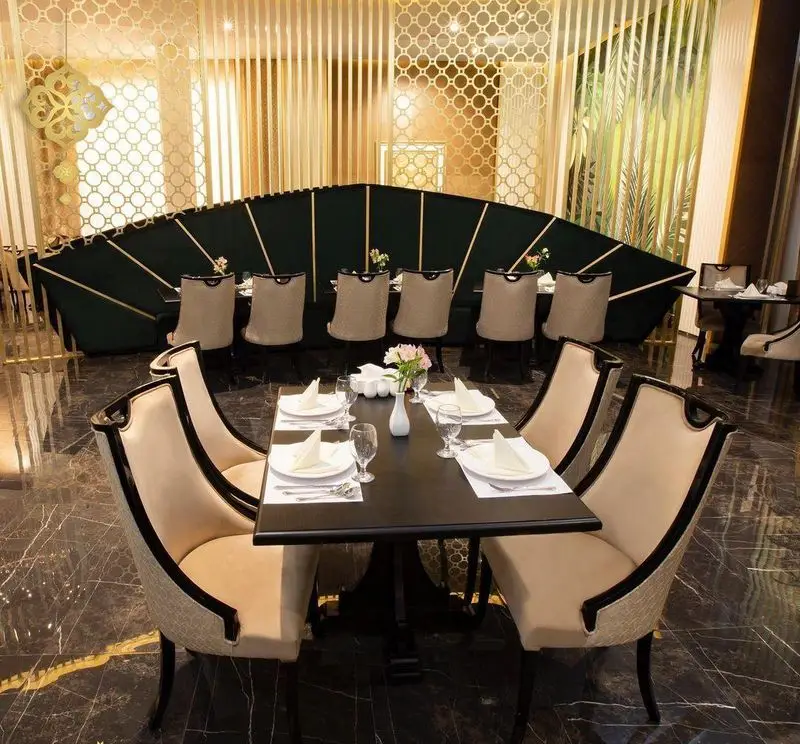 دکوراسیون شیک و مدرن رستوران ماهان شاندیز شریعتی با میزهای غذاخوری آماده، صندلی‌های زیبا و پارتیشن‌های طلایی.