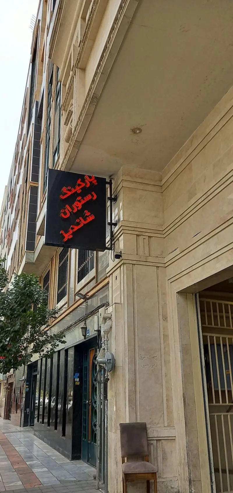 تصویری از نمای بیرونی رستوران ماهان شاندیز شریعتی در خیابان، شامل تابلوی راهنمای پارکینگ و ورودی با ساختمان سنگی.