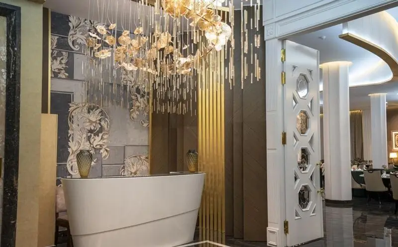 فضای داخلی لوکس و چشم‌نواز رستوران ماهان شاندیز شریعتی، شامل لوستر بزرگ طلایی، میز پذیرش مدرن و دکوراسیون دیوار منحصر به فرد.