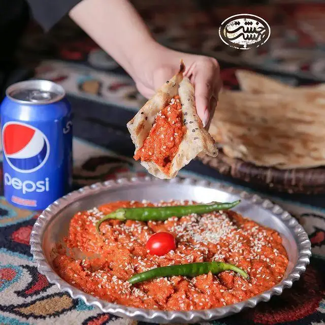 غذای سنتی خاص کافه رستوران خشت بهشت با مایه قرمز رنگ، فلفل سبز و کنجد، همراه نان سنگک و پپسی در محیط سنتی.
