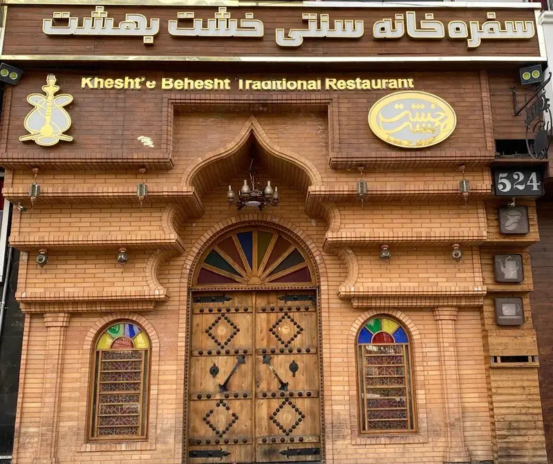 نمای ورودی کافه رستوران سنتی خشت بهشت با آجرکاری زیبا، درب چوبی بزرگ، شیشه‌های رنگی و تابلوی طلایی چشم‌نواز.