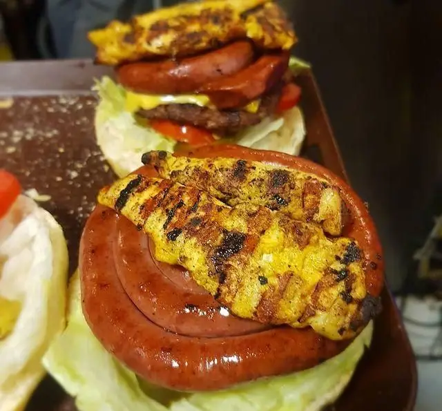 تصویری جذاب از ساندویچ‌های پرطرفدار فست فود برگریچ شامل برگر با سوسیس و پنیر، و ساندویچ سوسیس گریل با جوجه کباب زعفرانی بر روی کاهو.